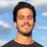 Michael Charlebois' headshot. He has short black hair and is wearing a black shirt. Behind him is the sky with clouds.