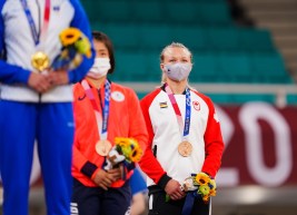 Jessica Klimkait stands with her bronze medal wearing her Team Canada jacket and mask.