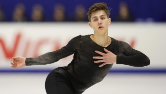 Roman Sadovsky holds his arm out and a hand to his chest while figure skating