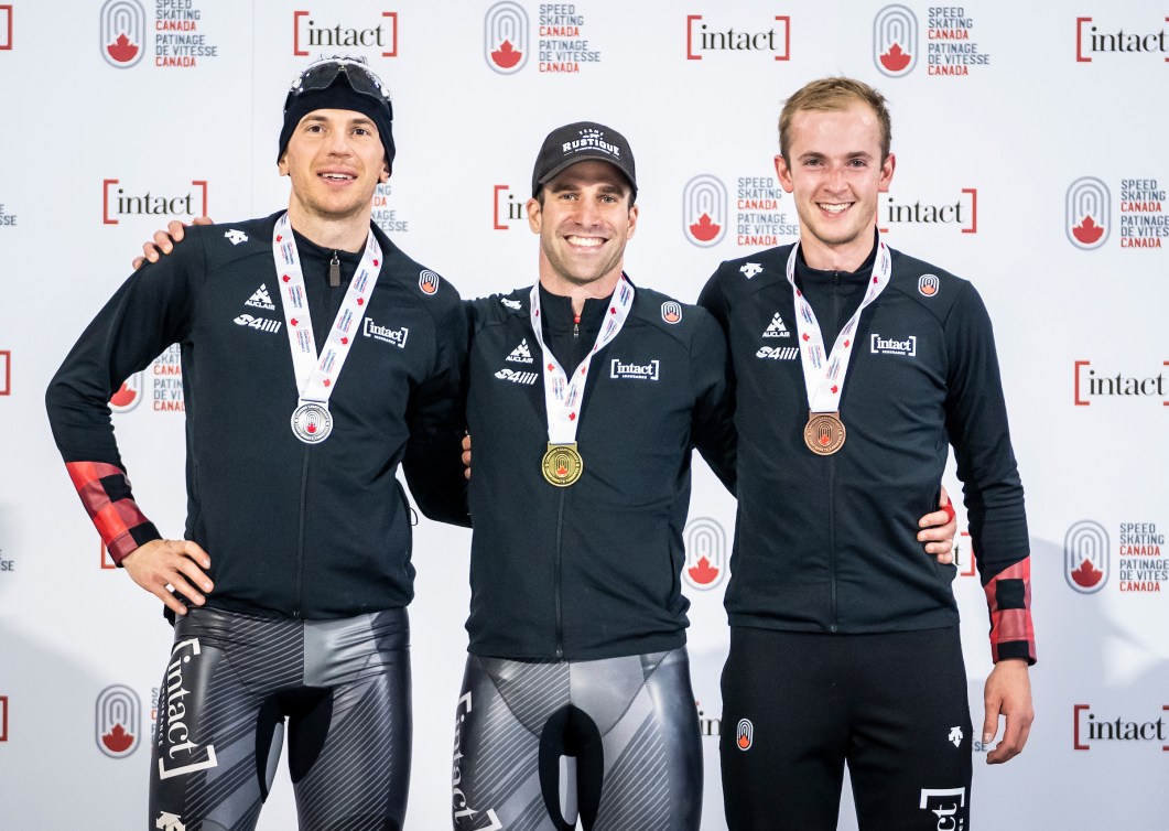 Three male speed skaters stand on a podium