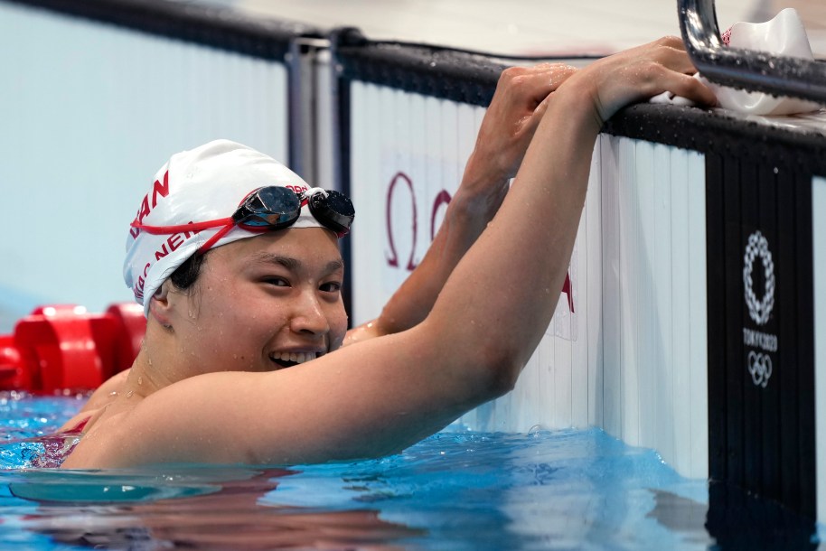Maggie Mac Neil rests her hands on the pool deck and smiles after winning the women's 100m race at Tokyo 2020.