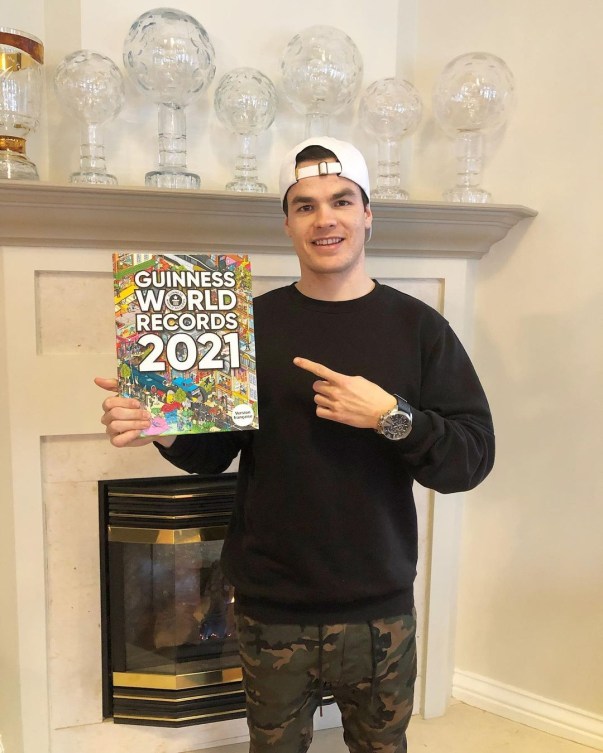 Mikaël Kingsbury holds up a copy of the 2021 edition of the Guiness Book of World Records. Behind him are some of his Crystal Globes on the fireplace mantle.