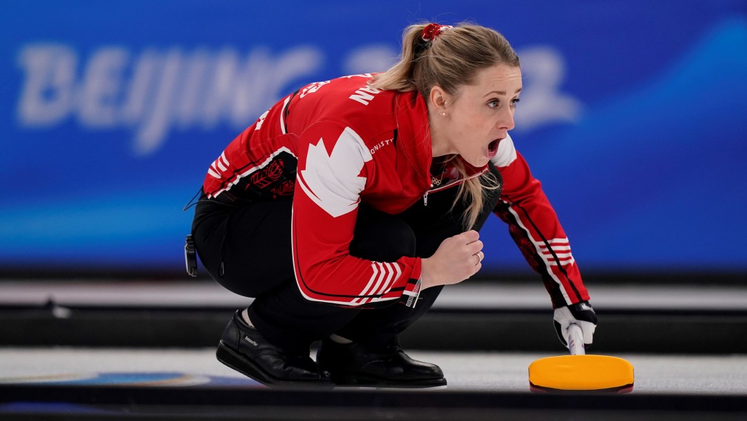 Wearing a red jacket and black pants Jocelyn Peterman yells at her teammates as she squats to watch her stone