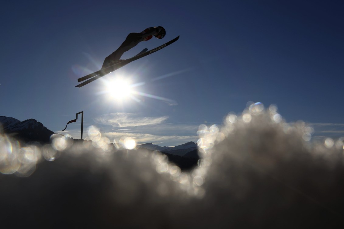 Side angle of a ski jumper soaring above clouds with the sun in background 