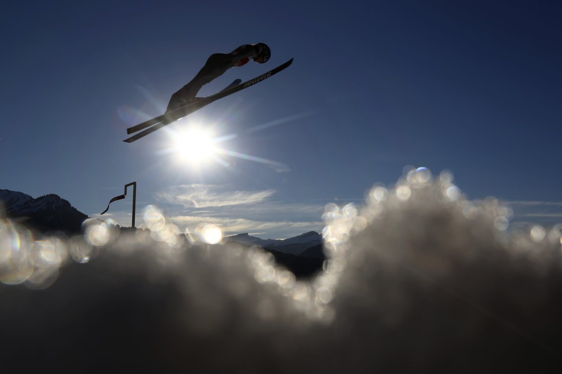 Side angle of a ski jumper soaring above clouds with the sun in background
