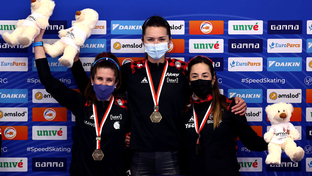 (left to right) Ivanie Blondin, Isabelle Weidemann and Valérie Maltais stand together for a group photo with their gold medals around their neck. They are each holding a white teddy bear.