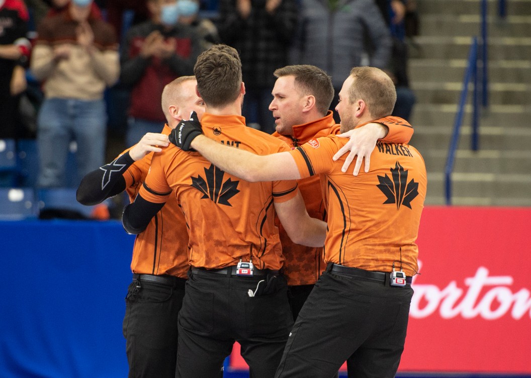 The four members of Team Gushue hug on the ice 