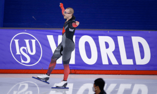 Speed skater raises hands in the air to celebrate victory on the ice