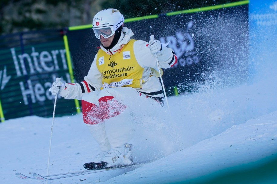 male athlete skis down a hill. There is snow flying up around him.