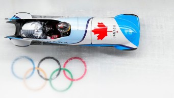 Canadian two-man bobsled goes past the Olympic rings on the ice