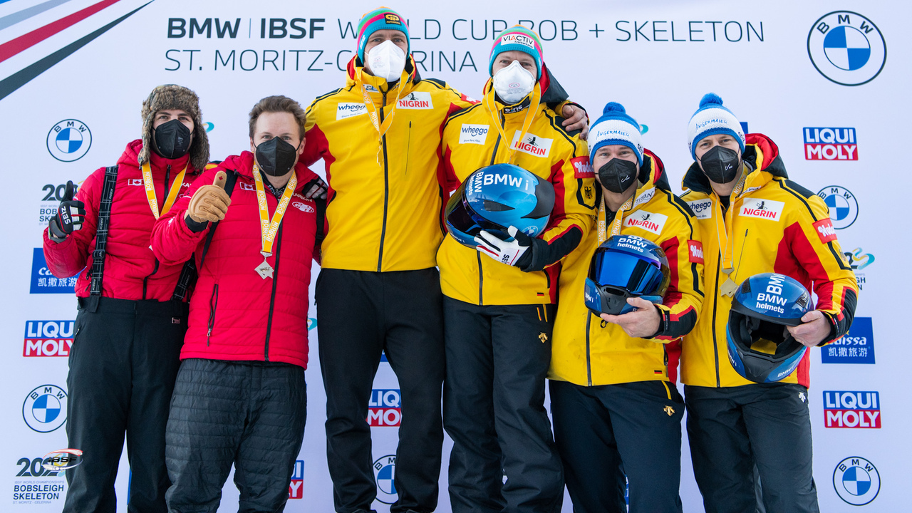 Three pairs of bobsleigh athletes pose for a picture on the podium with medals wrapped around their necks.