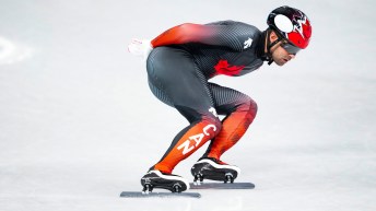 Speed skater in a red and black suit is bent at knees skating on the ice