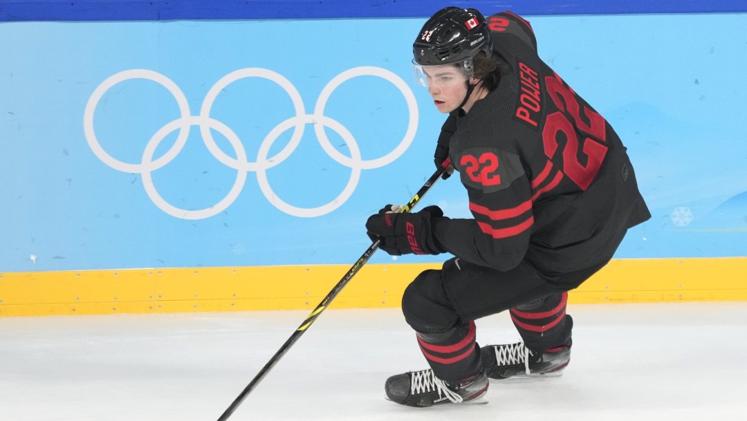 Owen Power skates by the Olympic rings on the boards