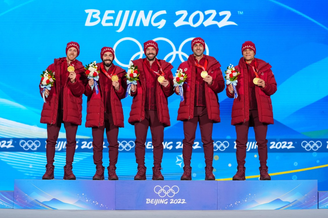 Short track speed skater relay members on podium wearing gold medals