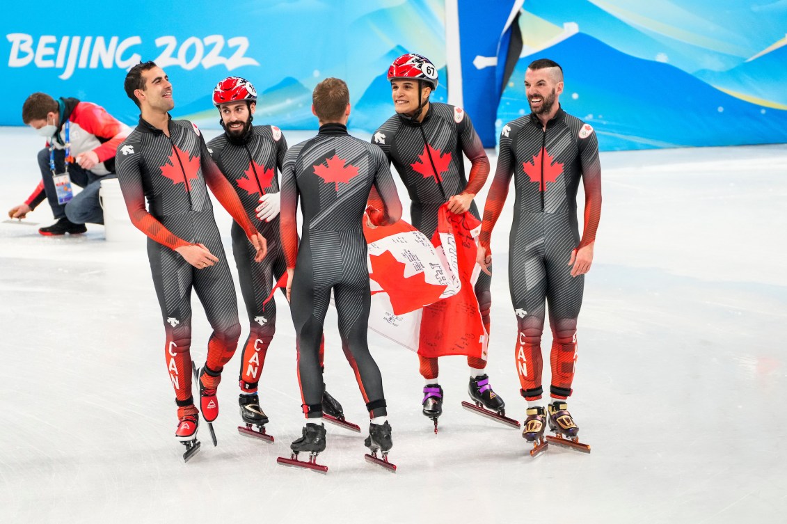 Canada's men's short track relay team hold the Canadian flag on the ice 