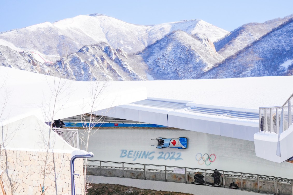 Wide shot of Christine de Bruin's bobsled on track with snowy mountains in background