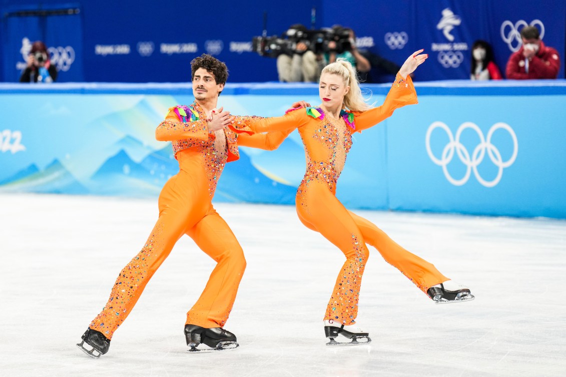 Piper Gilles and Paul Poirier skate in orange jumpsuits