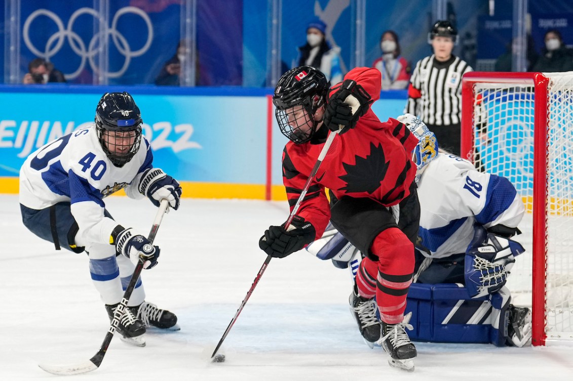 Sarah Fillier #10 of Team Canada tips the puck while avoiding a check by Noora Tulus #40 of Team Finland during the Beijing 2022 Olympic Winter Games