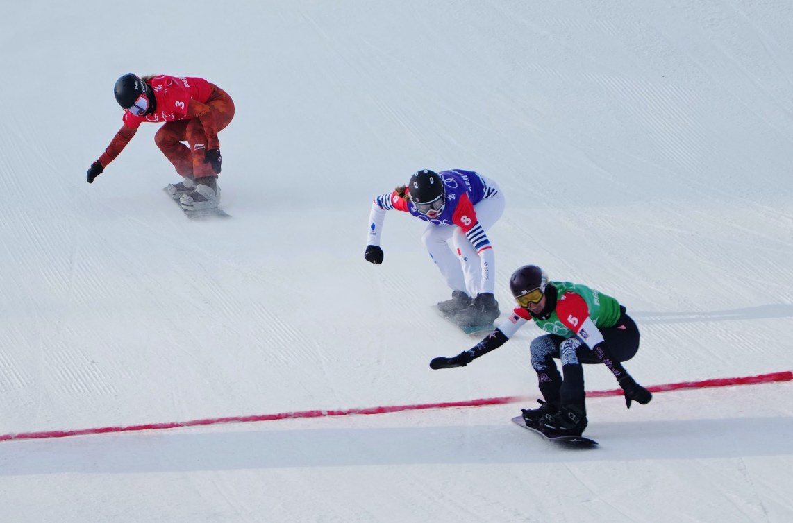 Three snowboaders race to the finish line in a snowboard cross race