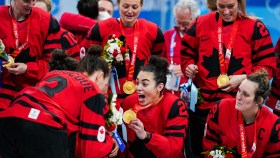 Sarah Nurse shows off her gold medal to teammates with a big grin