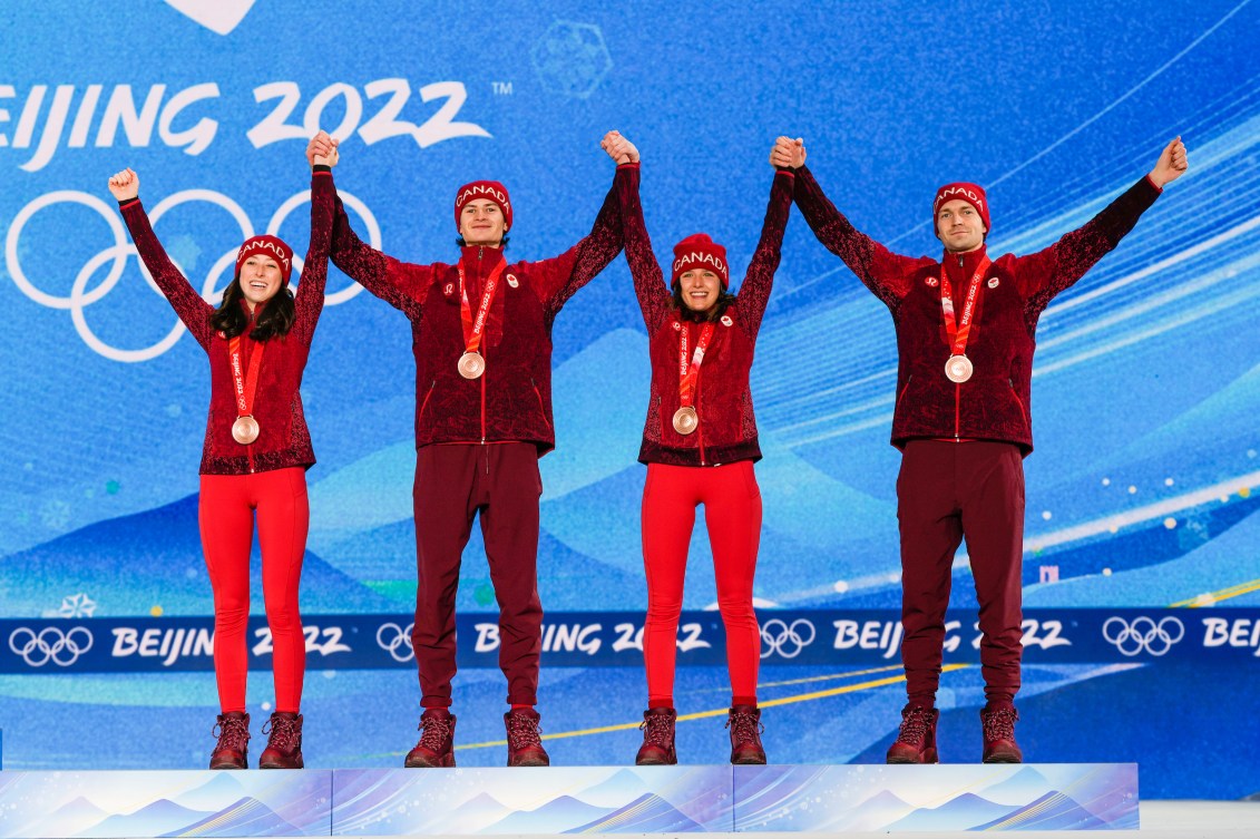 Four ski jumpers stand on the podium with arms raised
