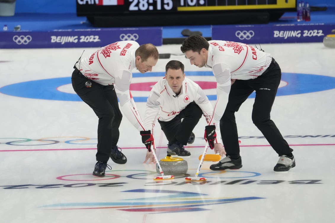 Brad Gushue throws a stone while Geoff Walker and Brett Gallant sweep