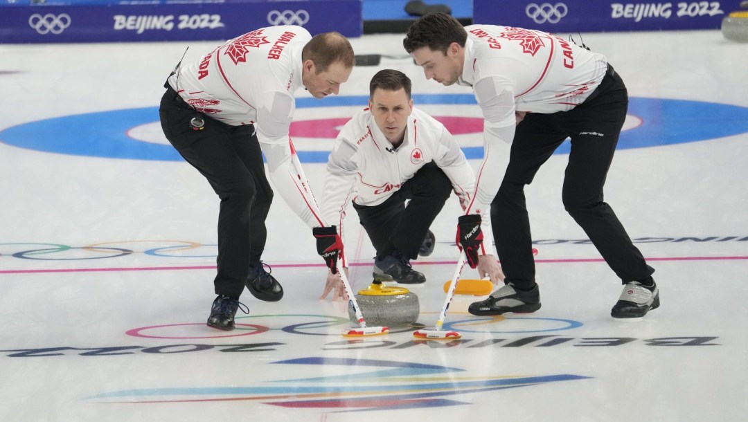 Brad Gushue throws a stone while Geoff Walker and Brett Gallant sweep
