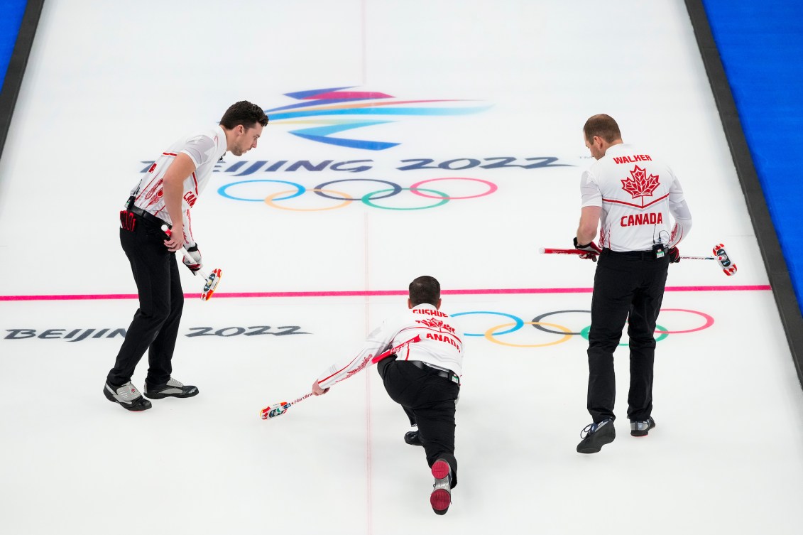 Back angle of Brad Gushue throwing and his sweepers ready to go