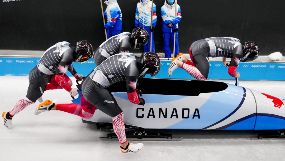 Side angle of four bobsledders running and pushing a sled