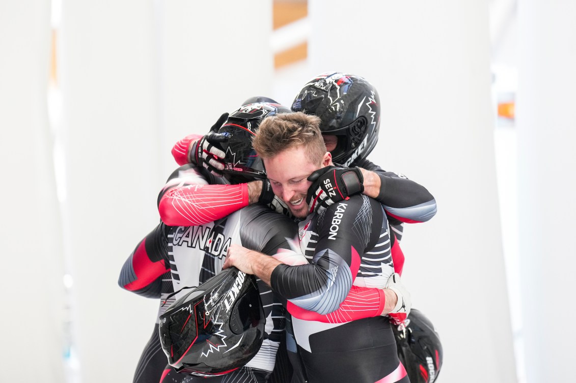 Four bobsledders hug after winning a medal 
