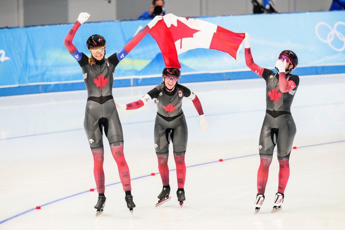 Isabelle Weidemann, Ivanie Blondin and Valerie Maltais carry the Canadian flag on a victory lap at the speed skating oval
