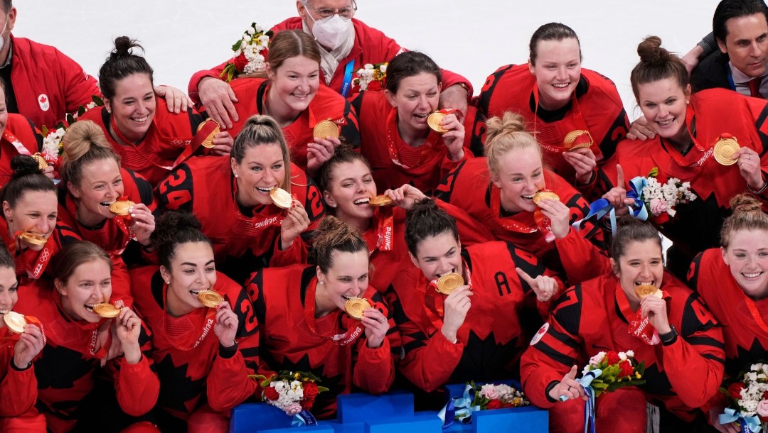 Members of Canada's women's hockey team bite their Olympic gold medals on the ice in Beijing