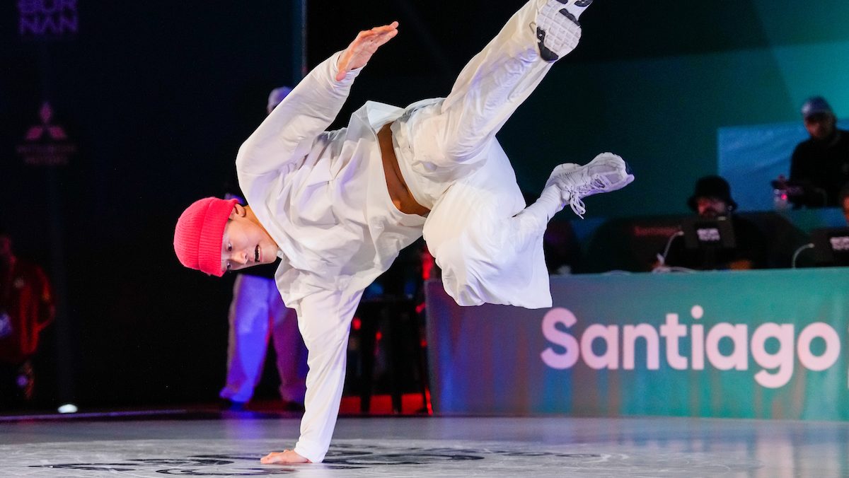 Phil Wizard in a white outfit and pink hat performs a dance move on one hand