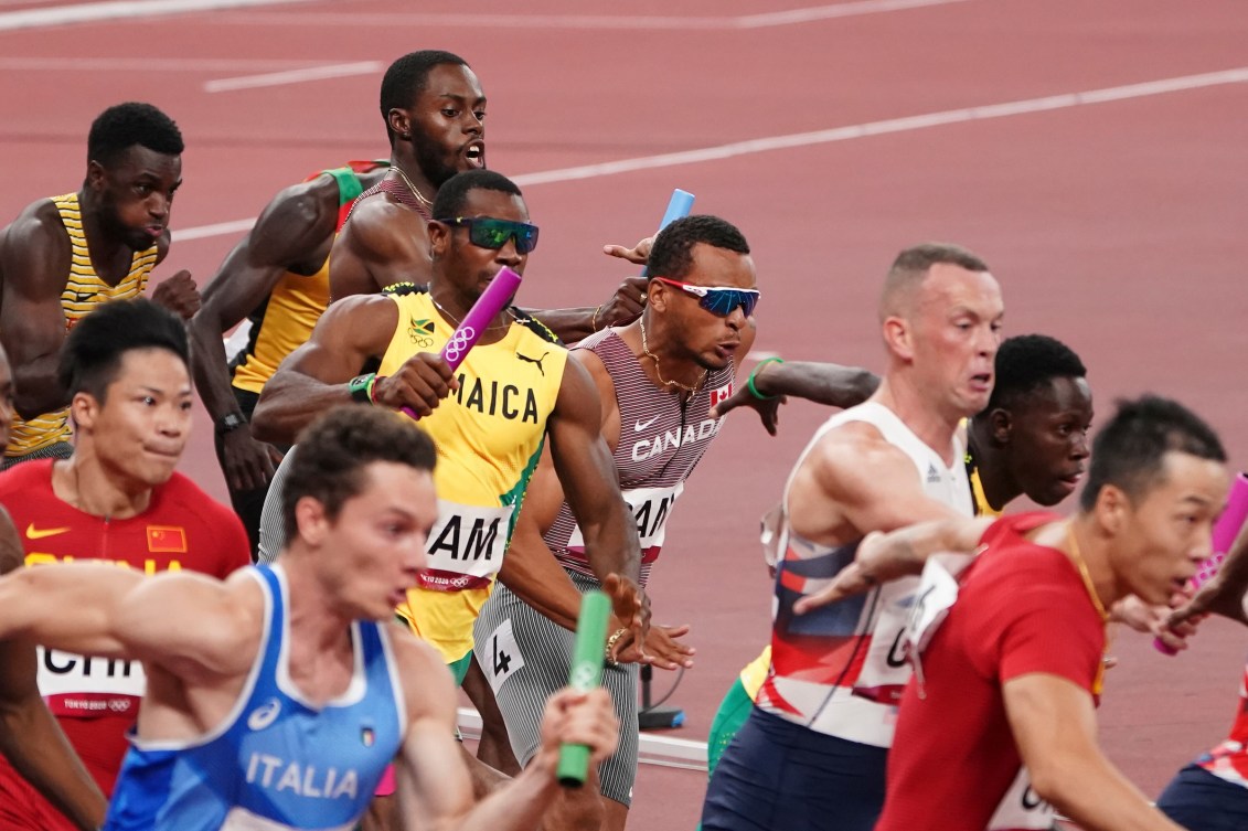 A lot of male sprinters make baton exchanges in a relay race 