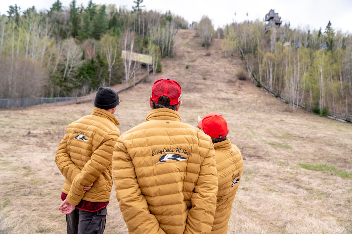 Three people stand back to camera as they look at the overgrown ski jumps at Big Thunder