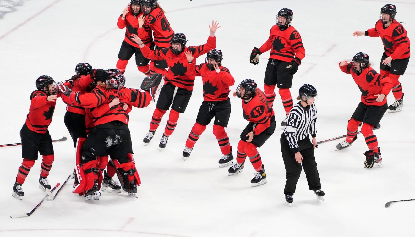Canadian women's hockey players prepare to jump on their goaltender in celebration 