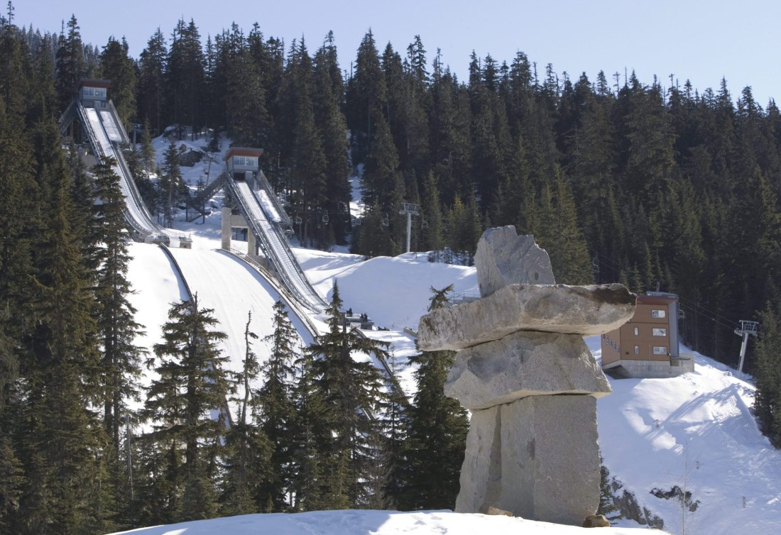 Wide scenic of two ski jump hills with Inukshuk in foreground