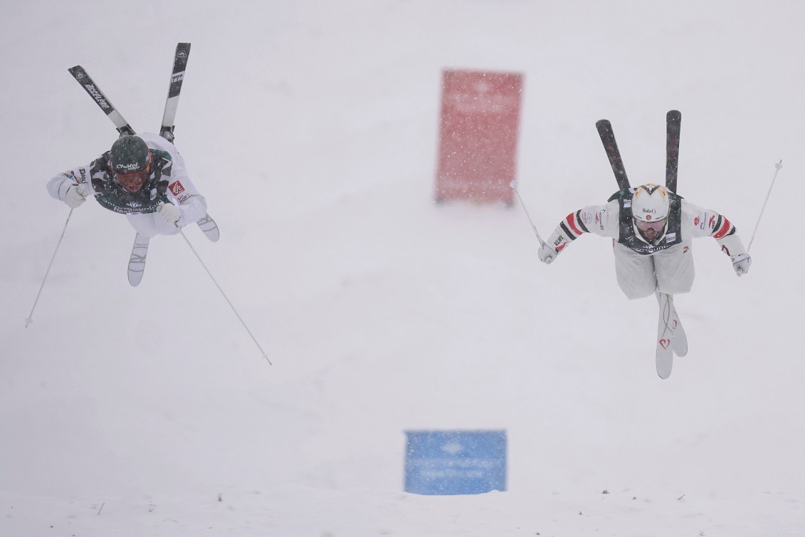 Two moguls skiers perform flips in the air while racing head to head 