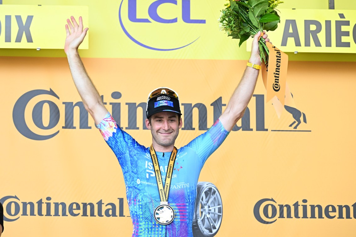 Hugo Houle wears a medal and holds a bouquet on the Tour de France podium