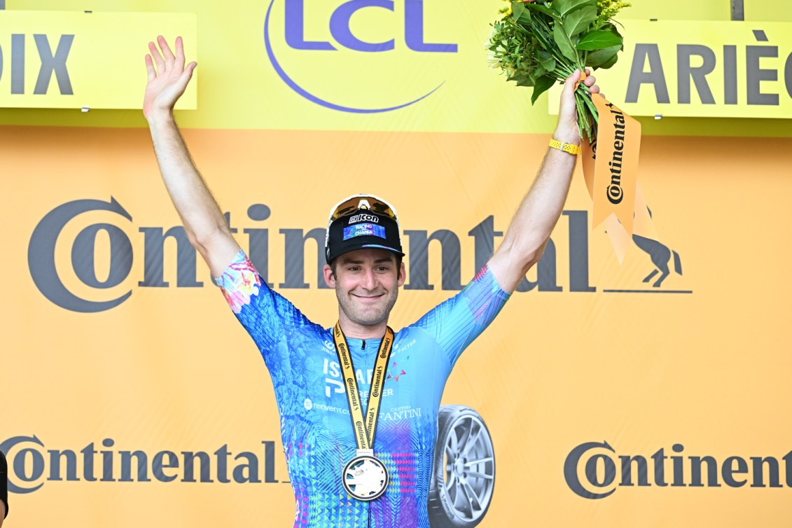 Hugo Houle luce una medalla y sostiene un ramo en el podio del Tour de Francia