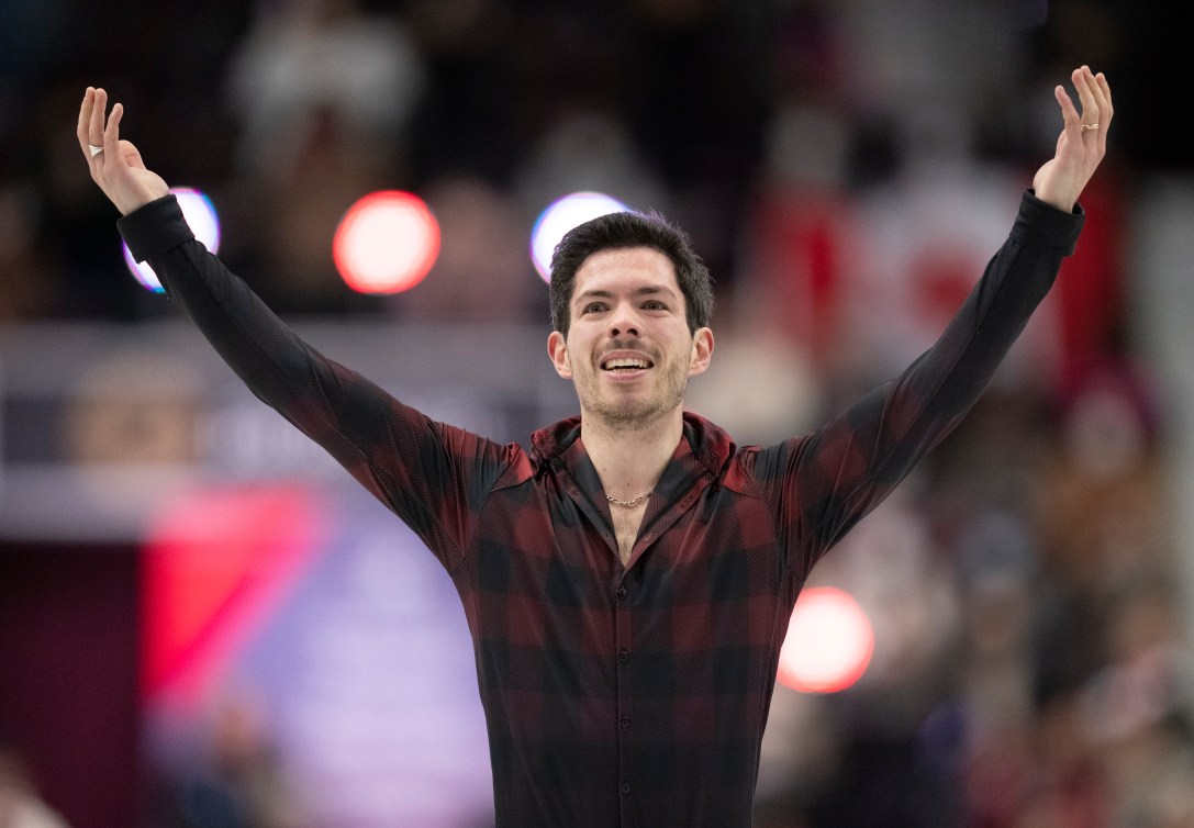 Keegan Messing in a plaid shirt raises his arms while smiling at the end of his performance 