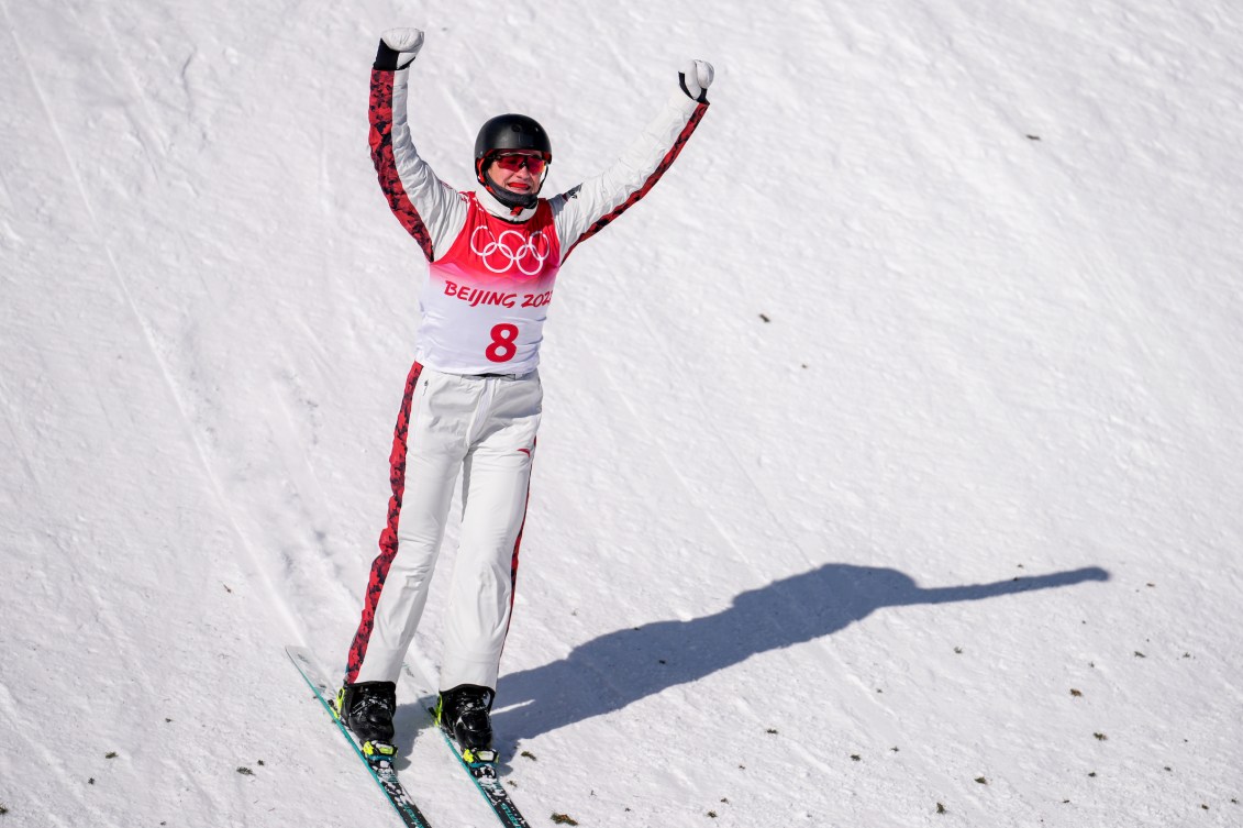 Marion Thenault raises her arms above her head after landing a jump on snow 
