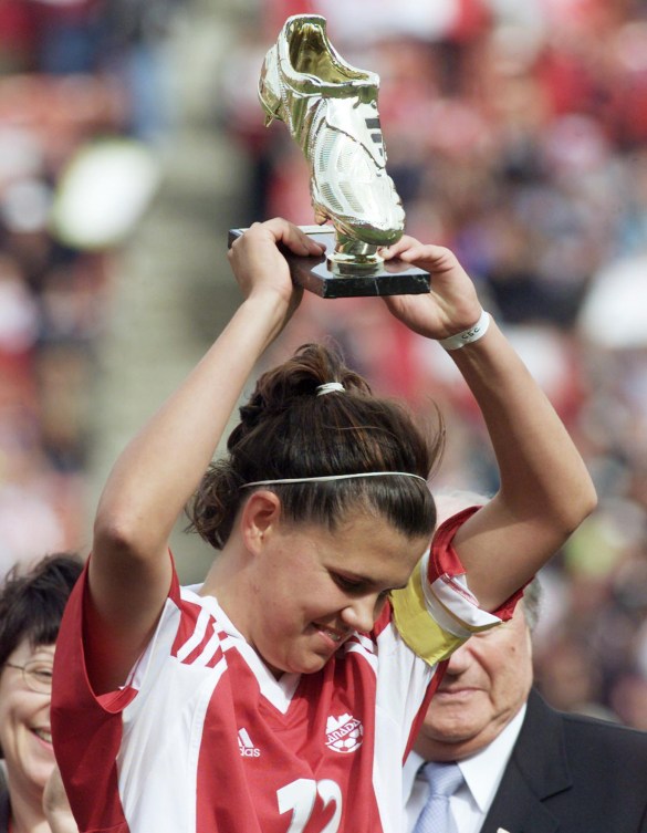 Chrtistine Sinclair holds a gold trophy of a soccer shoe above her head 
