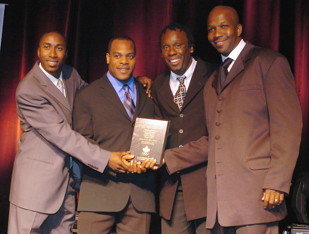 Four men in suits pose with a plaque
