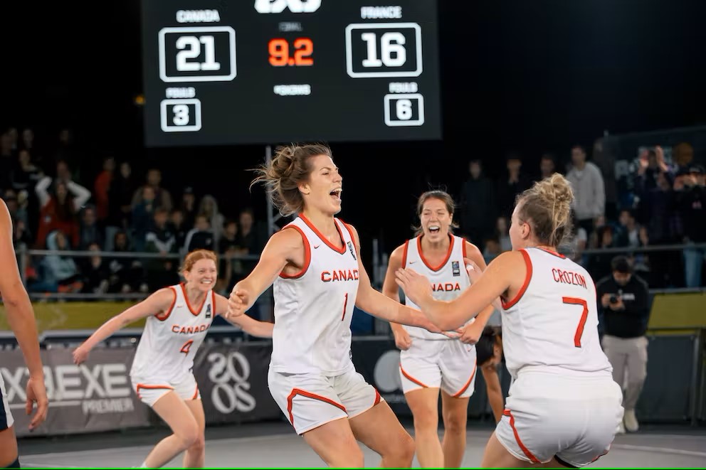 Four female basketball players in white about to jump and hug each other in celebration