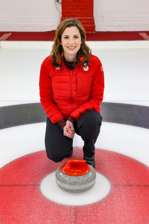 Lisa Weagle kneels next to a curling stone that has her name engraved on it 