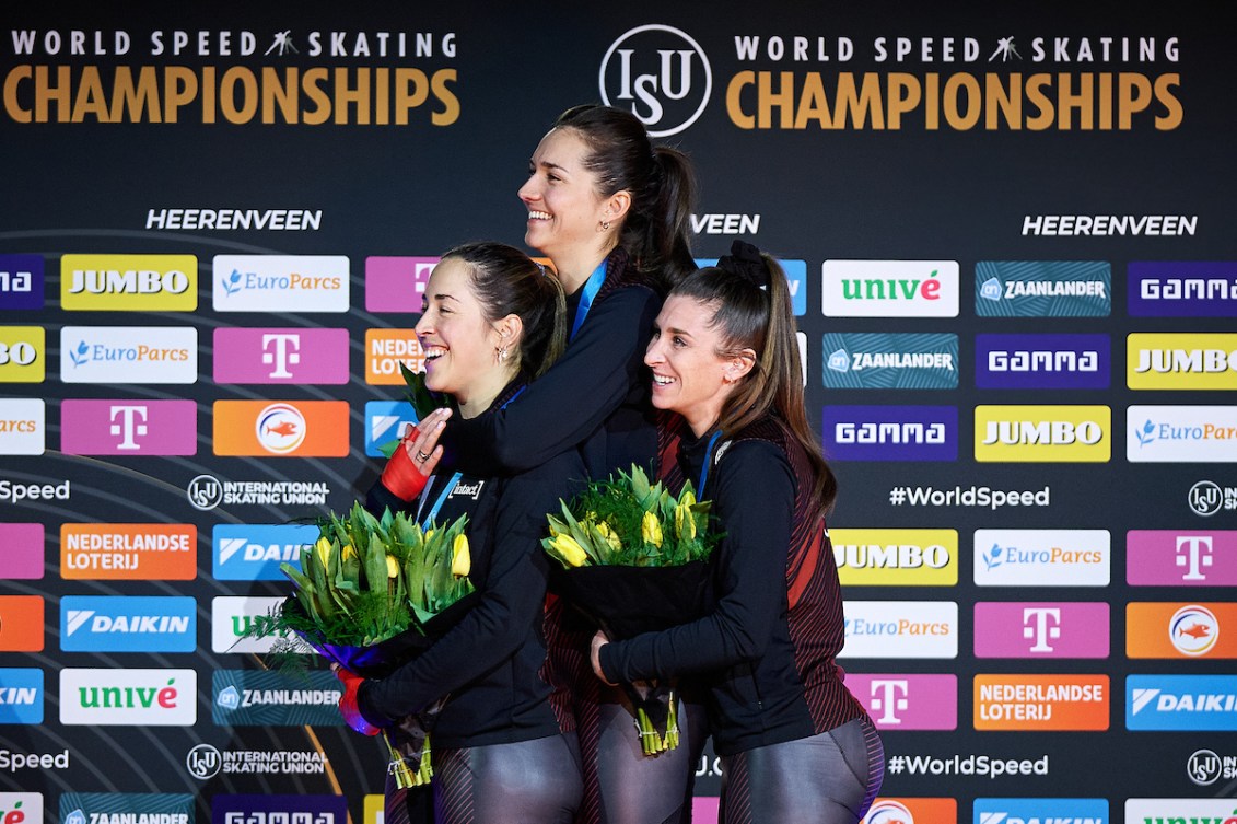 Three speed skaters hug each other on the podium