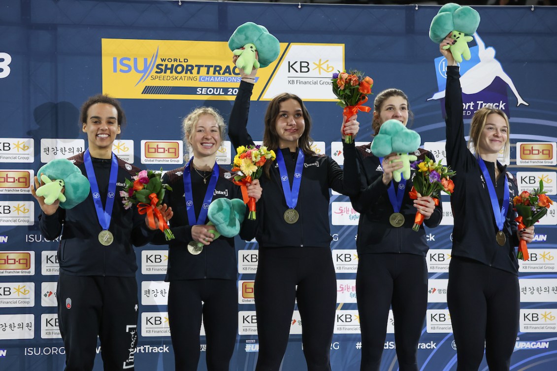 Five athletes wear medals and hold flowers on the podium 