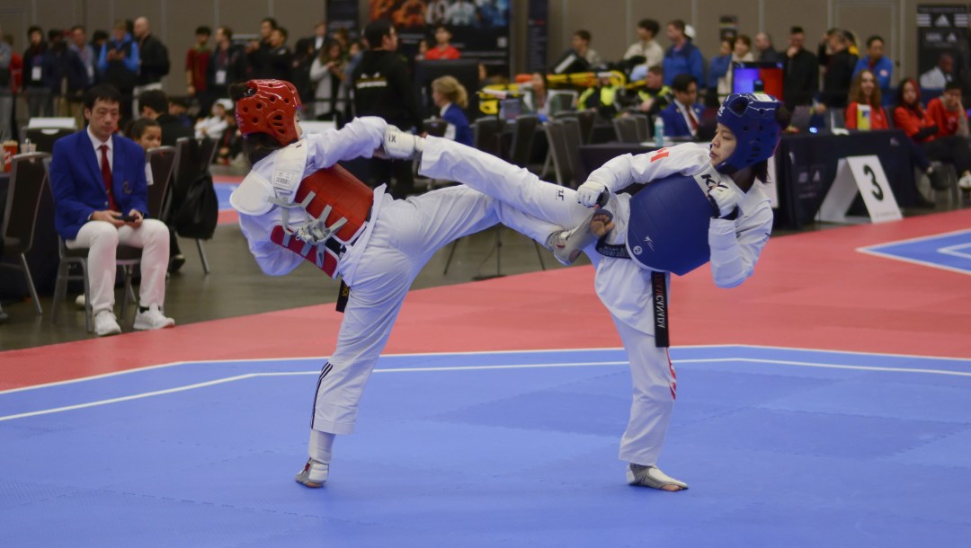 Angelique Orozco in a blue vest kicks her opponent in a taekwondo match.