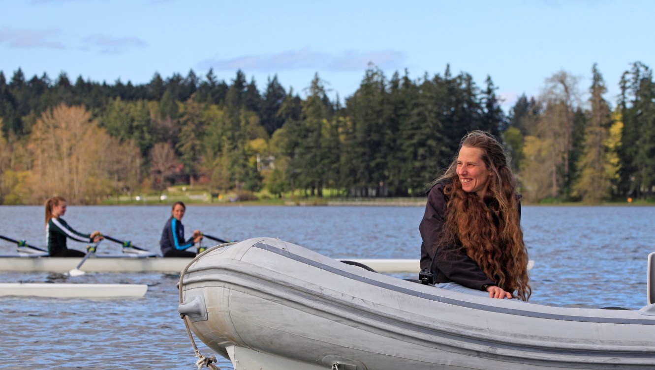 Brenda Taylor rides in a coach boat while rowers train on a lake